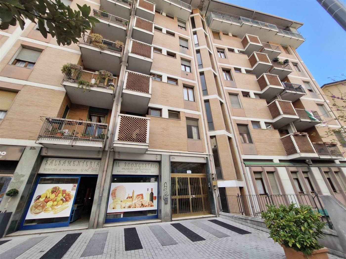 Palazzo residenziale in mattoni chiari con balconi a grata, al piano terra i negozi Salsamenteria e Il Buongustaio