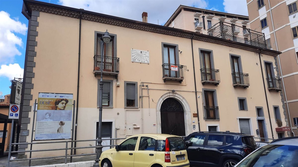 Palazzo storico beige con balconi in ferro battuto, portone ad arco, meridiana e manifesto «Eleonora Duse» sulla facciata