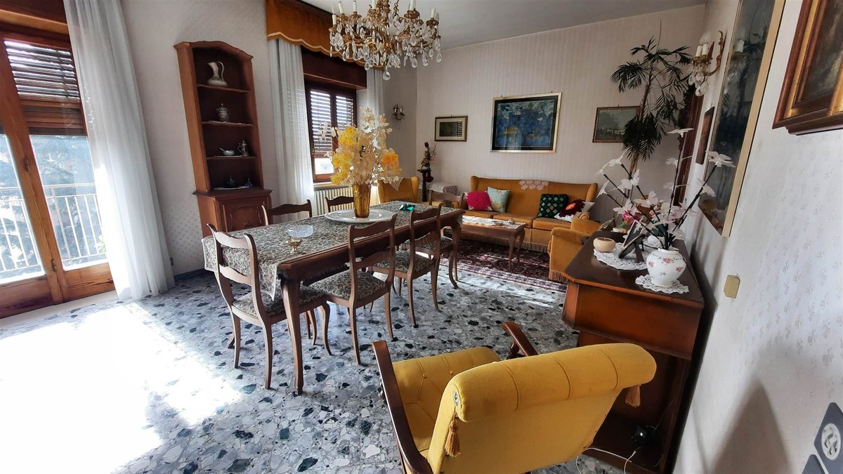 Soggiorno con tavolo da pranzo, poltrona gialla, divano ocra, lampadario di cristallo e pavimento in graniglia